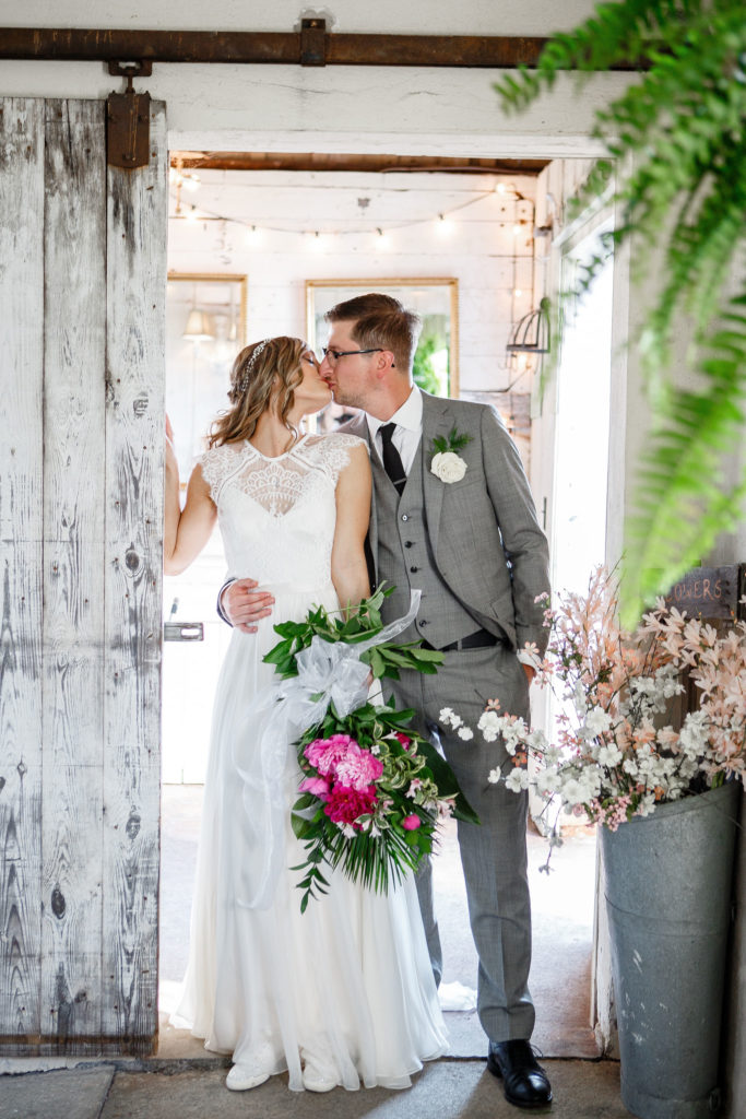 bride and groom kissing at barn door
