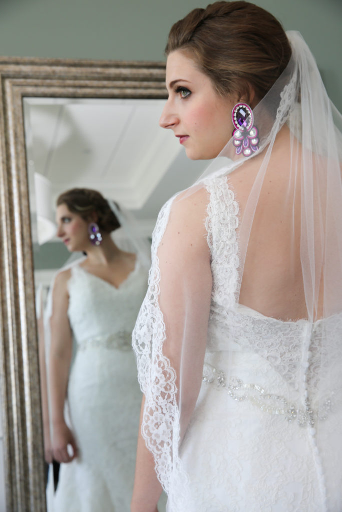 Bride posing in front of the mirror with a veil and big plum earrings