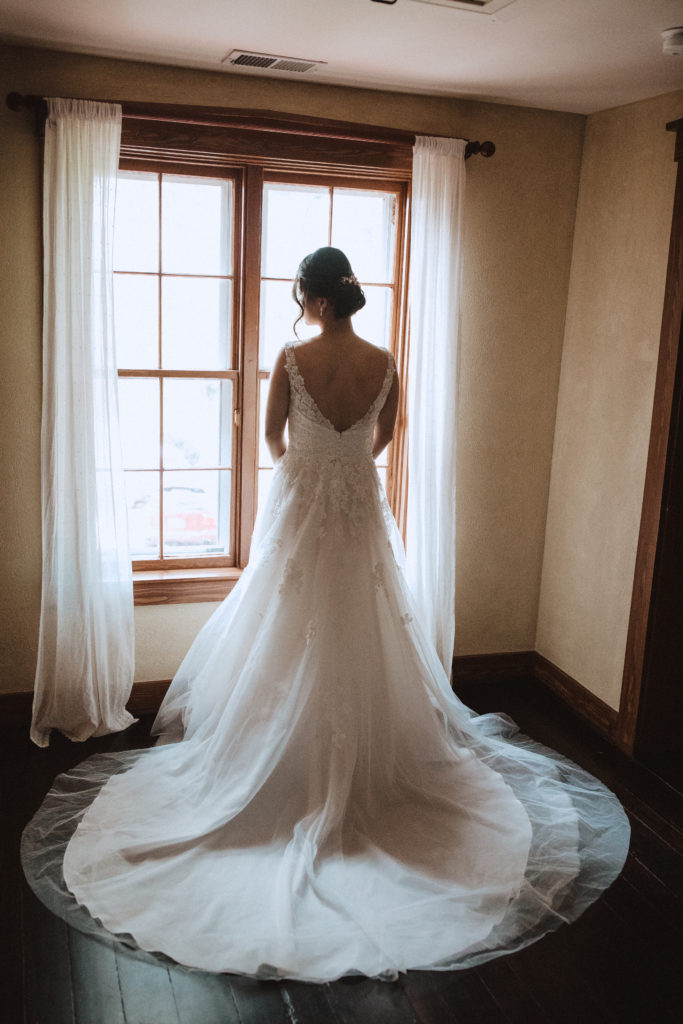 Bride with wedding dress looking at the window in farm house