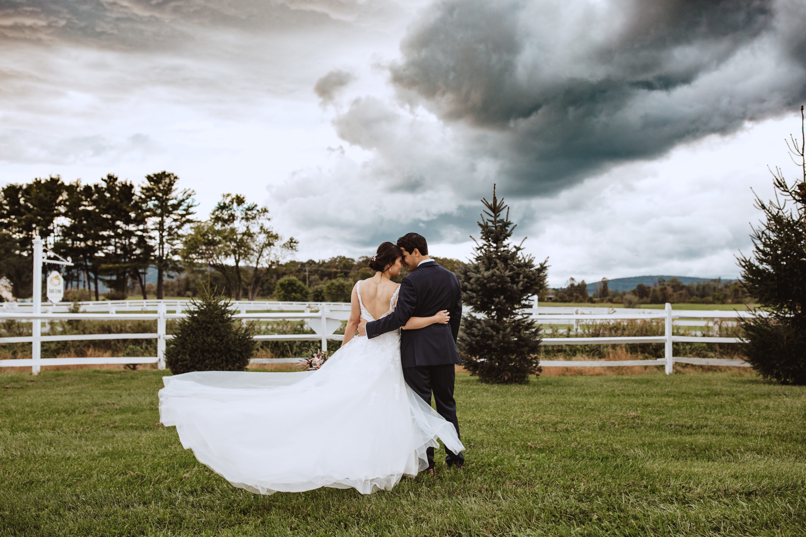 bride and groom backs hugging with clouds behing them